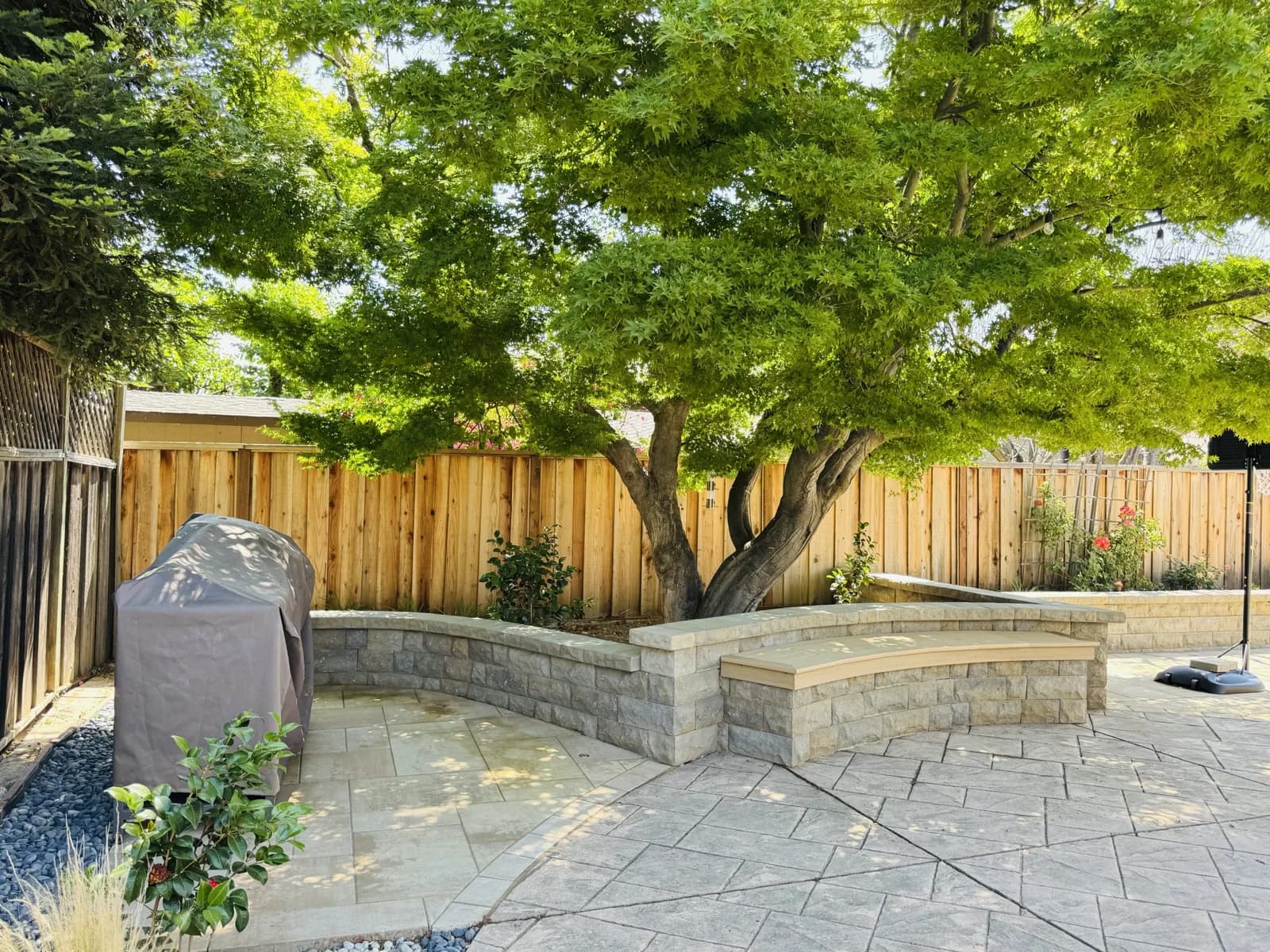 Curved block seat wall on a paver patio under a mature tree