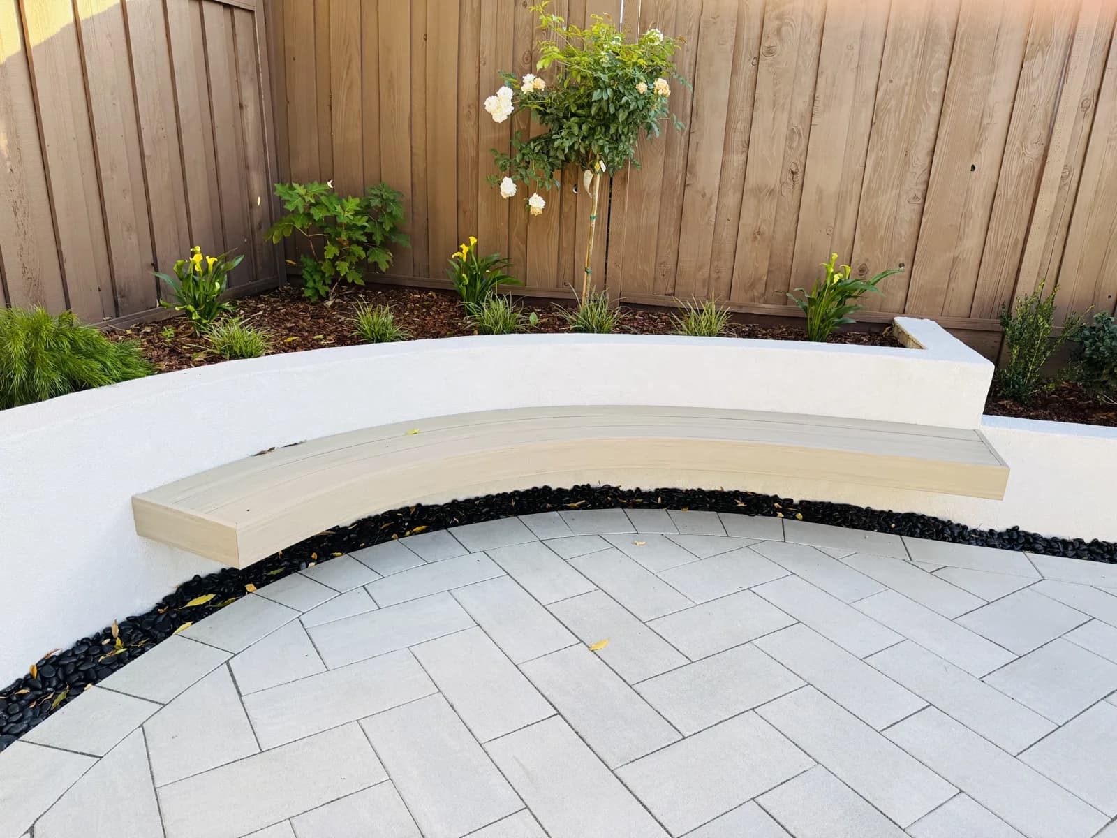 Curved floating bench on a white seat wall over large-format porcelain pavers