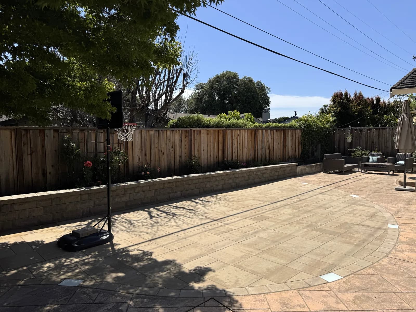 Paver patio with an in-ground basketball hoop and a low block retaining wall
