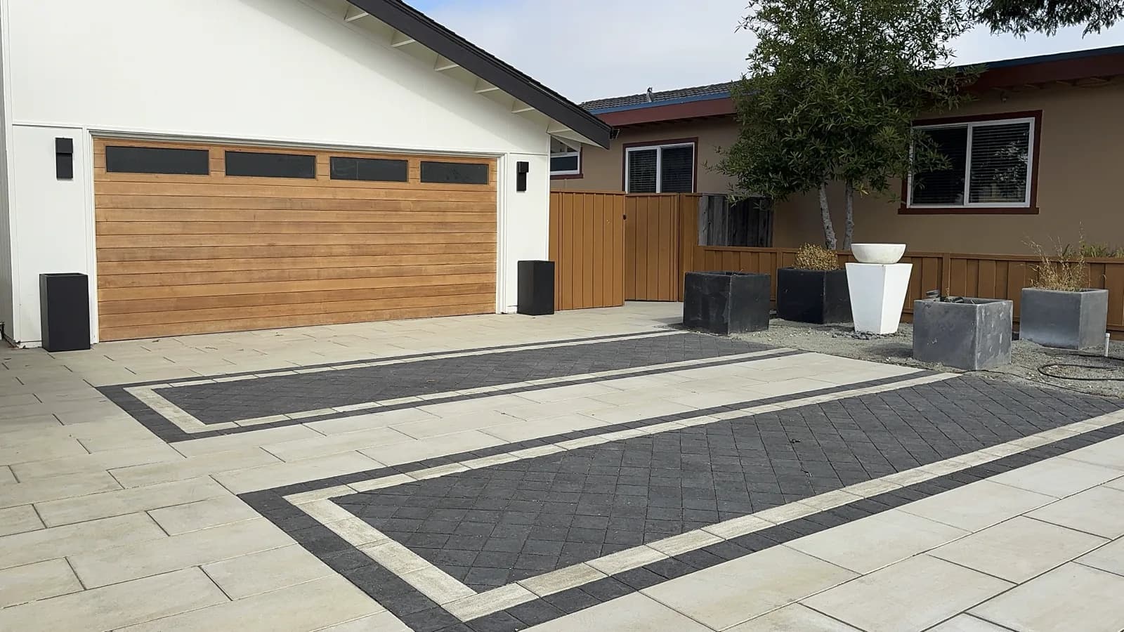 Paver driveway with dark herringbone inlay panels and a light border in front of a wood garage door