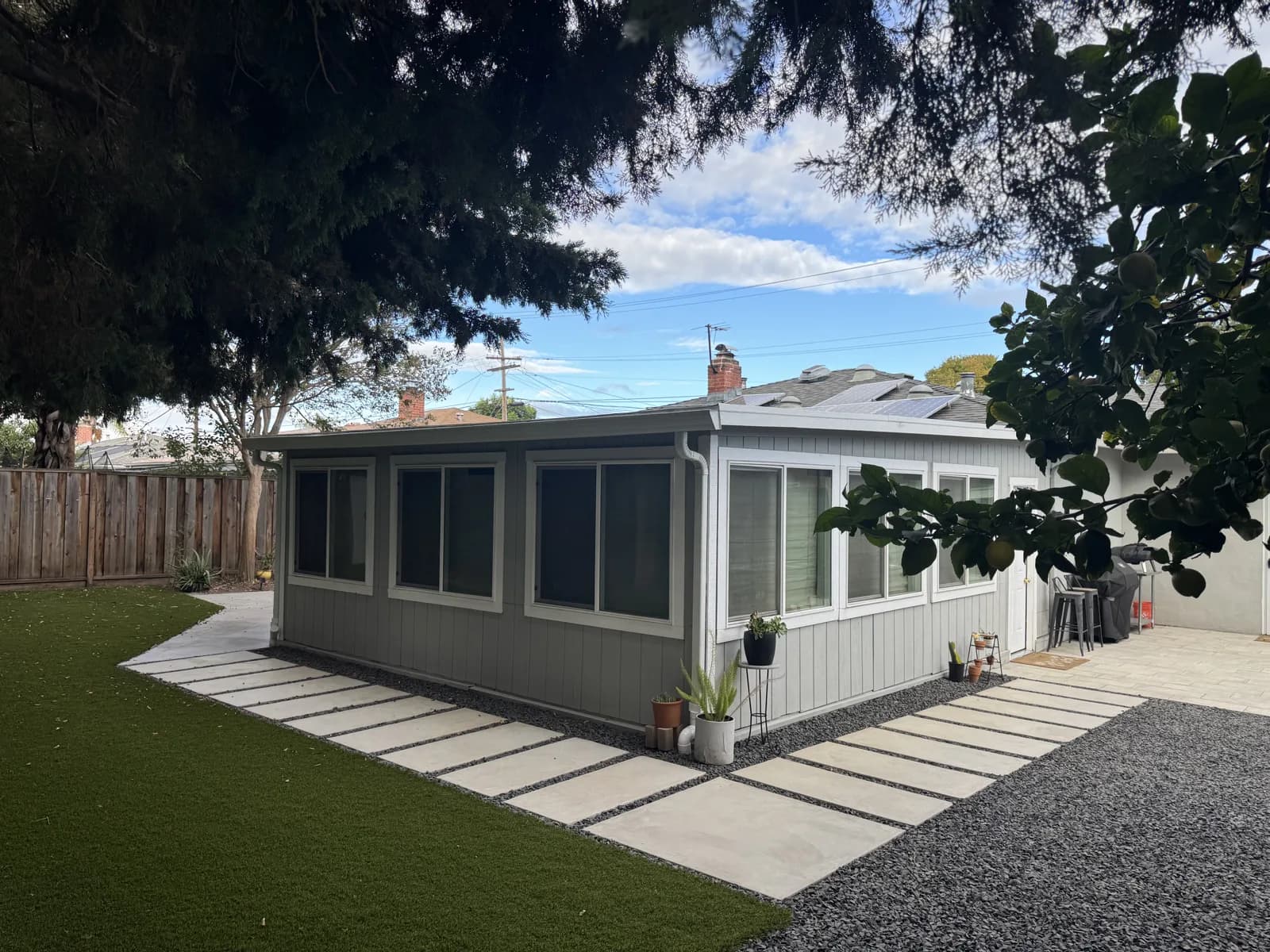 Concrete stepping pads in gravel and artificial turf wrapping around a garden room